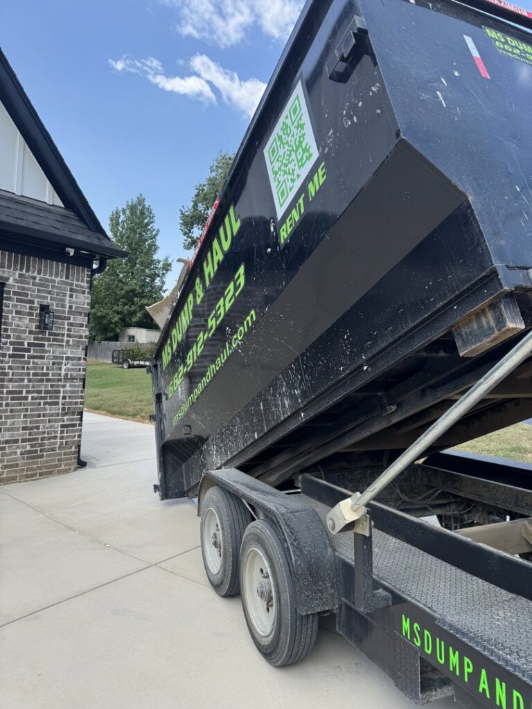 An MS Dump & Haul dumpster being tilted to unload debris on a residential driveway in Hernando, MS.