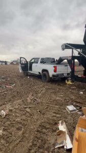 An MS Dump & Haul truck pulling a dumpster trailer at a muddy, debris-strewn job site in Hernando, MS.
