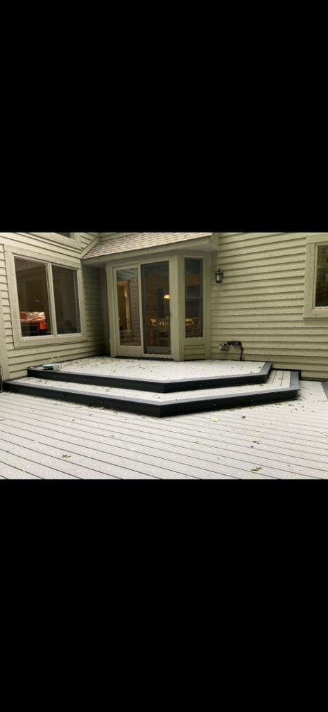 A multi-level composite deck featuring custom steps leading to a sliding glass door by Nader Builders in Ann Arbor, MI.