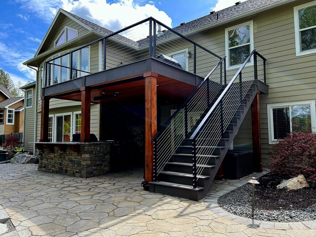 A multi-level finished deck with cable railing and stairs, seamlessly integrated with a stone patio by Ridgeline Decks in Spokane, WA.