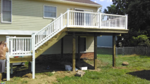 A handyman constructing a multi-level wooden deck with white railings for Fence Me In And Decks Too in Glen Allen, VA.