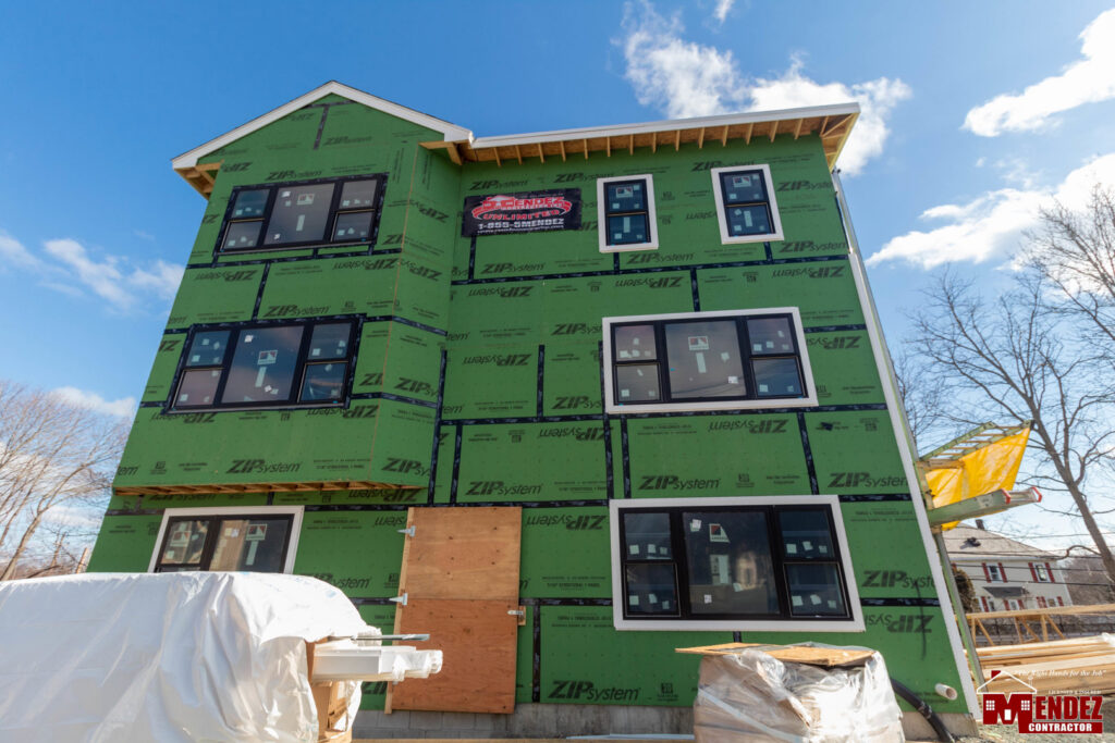 A multi-story building under construction with green sheathing and new windows by Mendez Contractor Inc in Lynn, MA