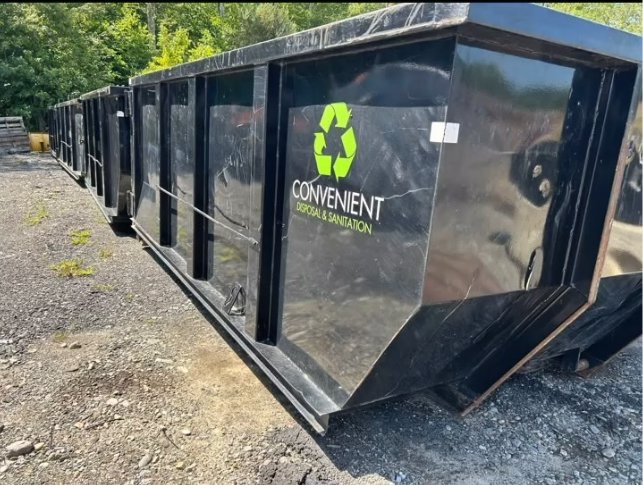 Several black dumpsters with the company logo stored in a gravel yard, ready for junk removal projects in Fall River, MA.
