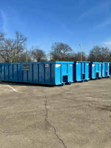 Multiple blue roll-off dumpsters from Ryan's Roll-Off Dumpsters lined up in a parking lot in Owensboro, KY.