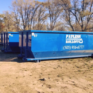 Several blue roll-off dumpsters from Payless Rolloff lined up in a dirt lot in Albuquerque, NM.