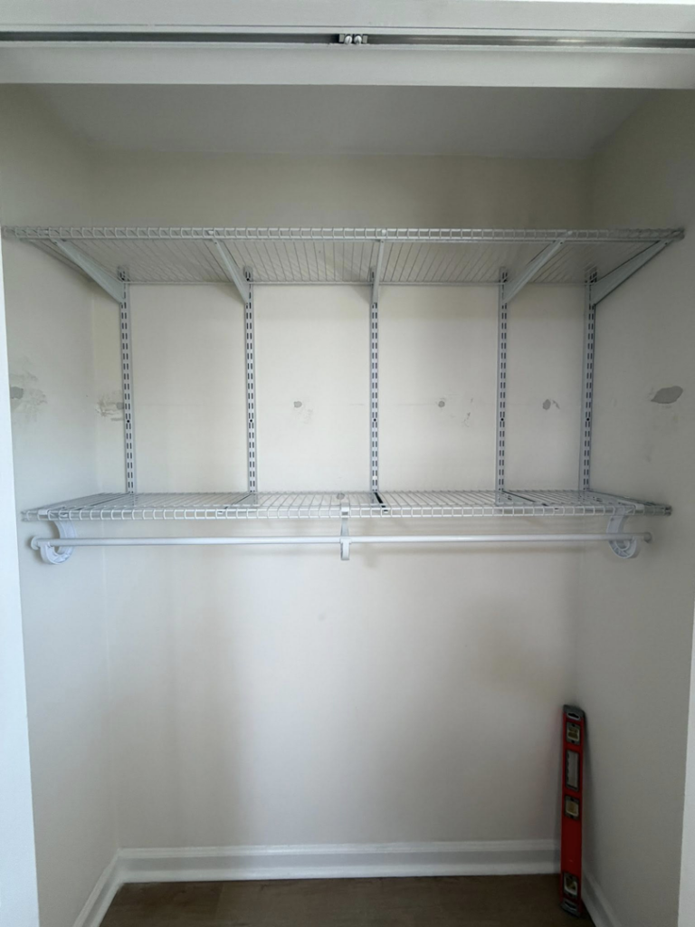 Multiple wire shelves installed in a closet, with a level on the floor, by HandyWorx Home Services LLC in Kenna, WV.
