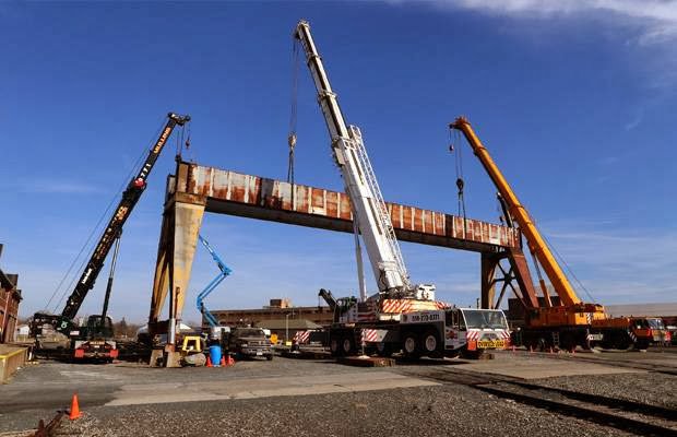 Multiple large cranes lifting a heavy steel structure at a job site, showcasing rigging expertise by Mullins Rigging in Green Island, NY