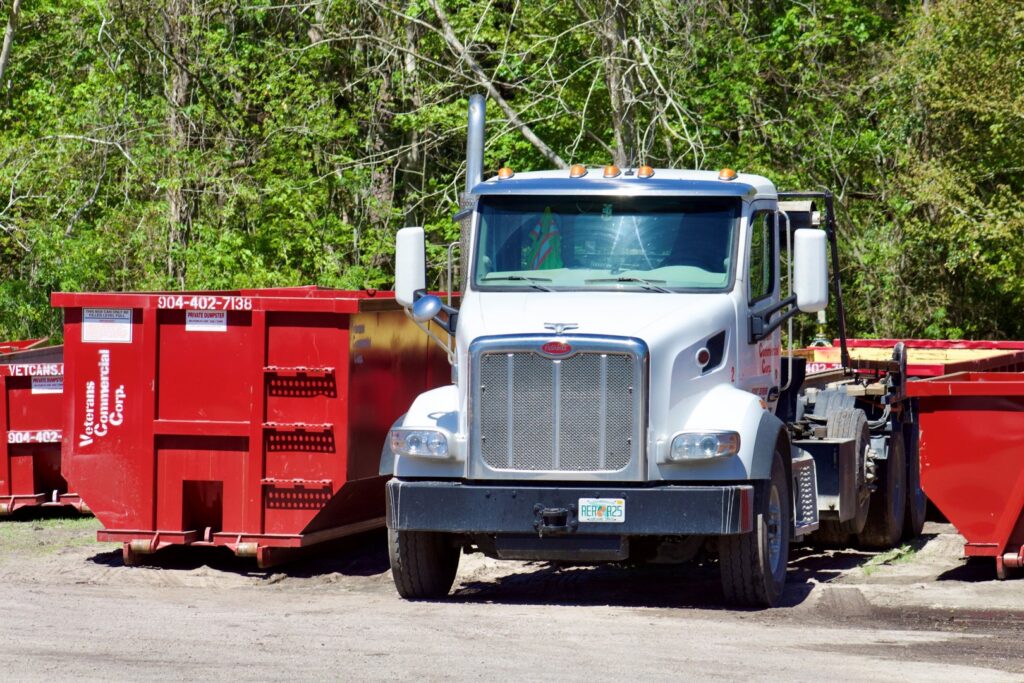 A Vetcans Dumpster Rental truck parked among several red dumpsters in a lot in Jacksonville, FL.