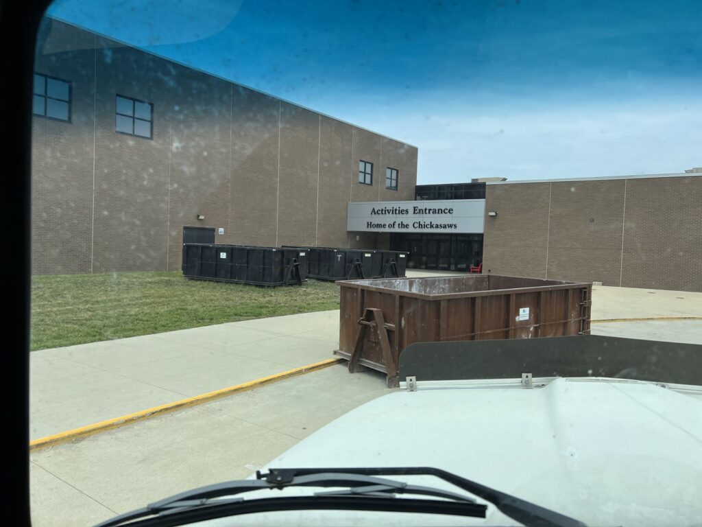 Multiple dumpsters provided by NID Dumpster Rental outside a school building in Nashua, IA for commercial waste.