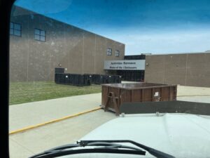 Multiple dumpsters provided by NID Dumpster Rental outside a school building in Nashua, IA for commercial waste.