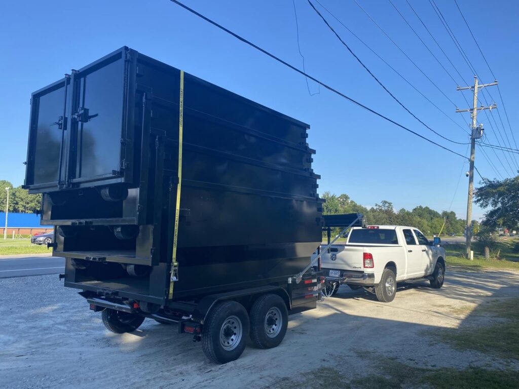 A white pickup truck towing a trailer loaded with multiple stacked dumpsters for The Dumpster Dad in Wilmington, NC.