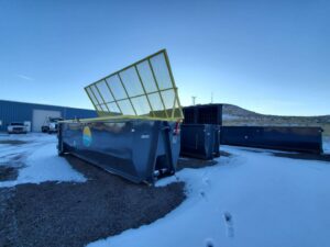 Multiple roll-off dumpsters, one with an open safety net, stored by First Light Services Llc in Casper, WY.