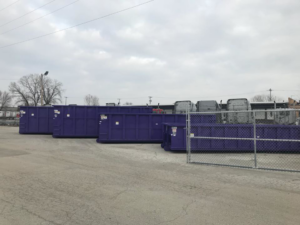 Multiple purple roll-off dumpsters from Rock Acres Companies parked in a lot in Kansas City, MO.