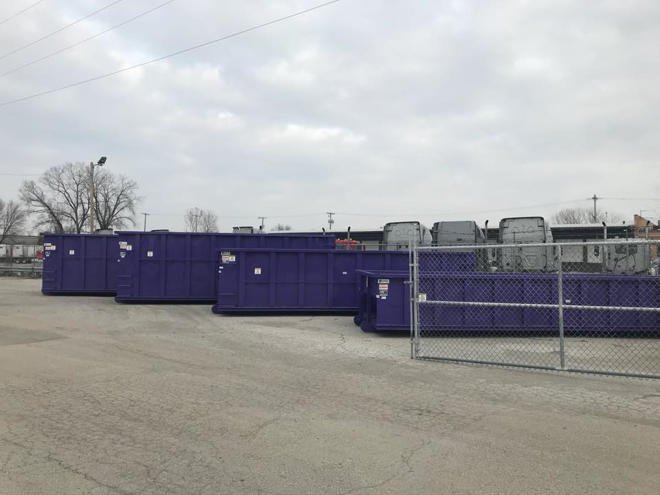 Multiple purple roll-off dumpsters from Rock Acres Companies parked in a lot in Kansas City, MO.