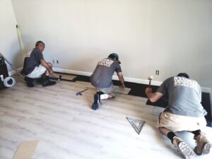 A team of three workers from Stormtroopers Home Improvement installing light wood-look flooring as part of a home renovation in Port St. Lucie, FL.