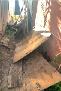 A narrow outdoor area with broken wooden boards and debris, indicating a cleanup job for Roadrunner JunkSmart Solutions LLC in Las Cruces, NM.