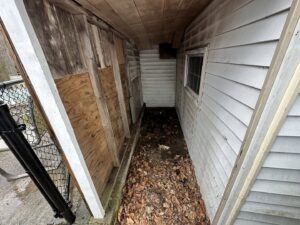 A narrow space between two buildings filled with leaves and debris, indicating a cleanout job for CK Junk Removal in New Bedford, MA