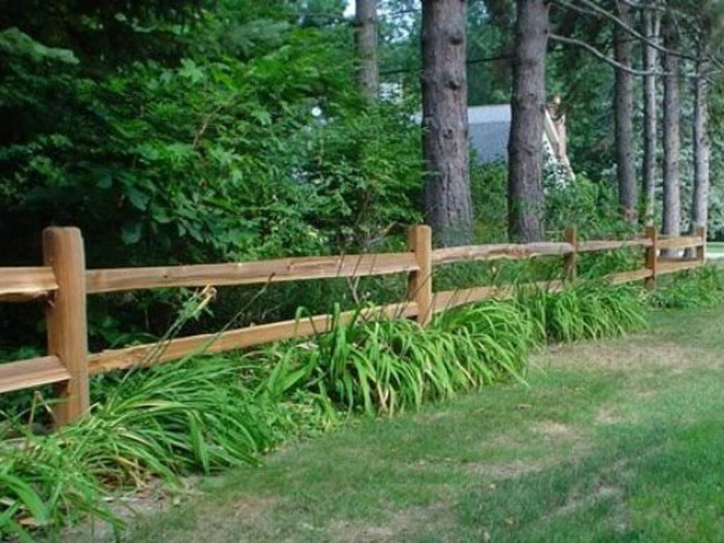 A natural wood split-rail fence with lush greenery, showcasing fence installation by Steven's Deck and Fence Staining Columbus, GA.