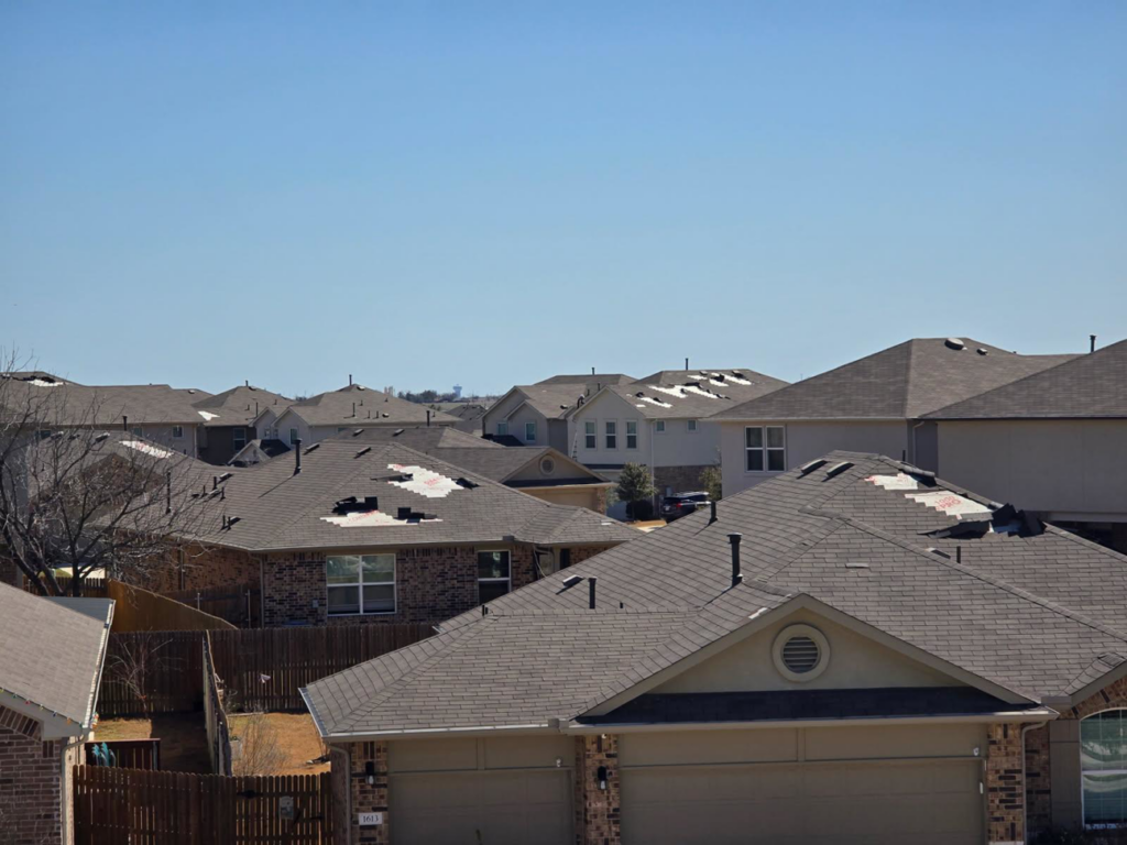 Aerial view of a neighborhood with damaged roofs and exposed underlayment, showing roof repair by APEX Roofing in Georgetown, TX.
