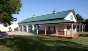 A newly constructed barn-style building with a green metal roof and a wrap-around porch by D.H. Construction in Jackson, TN.