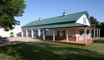 A newly constructed barn-style building with a green metal roof and a wrap-around porch by D.H. Construction in Jackson, TN.