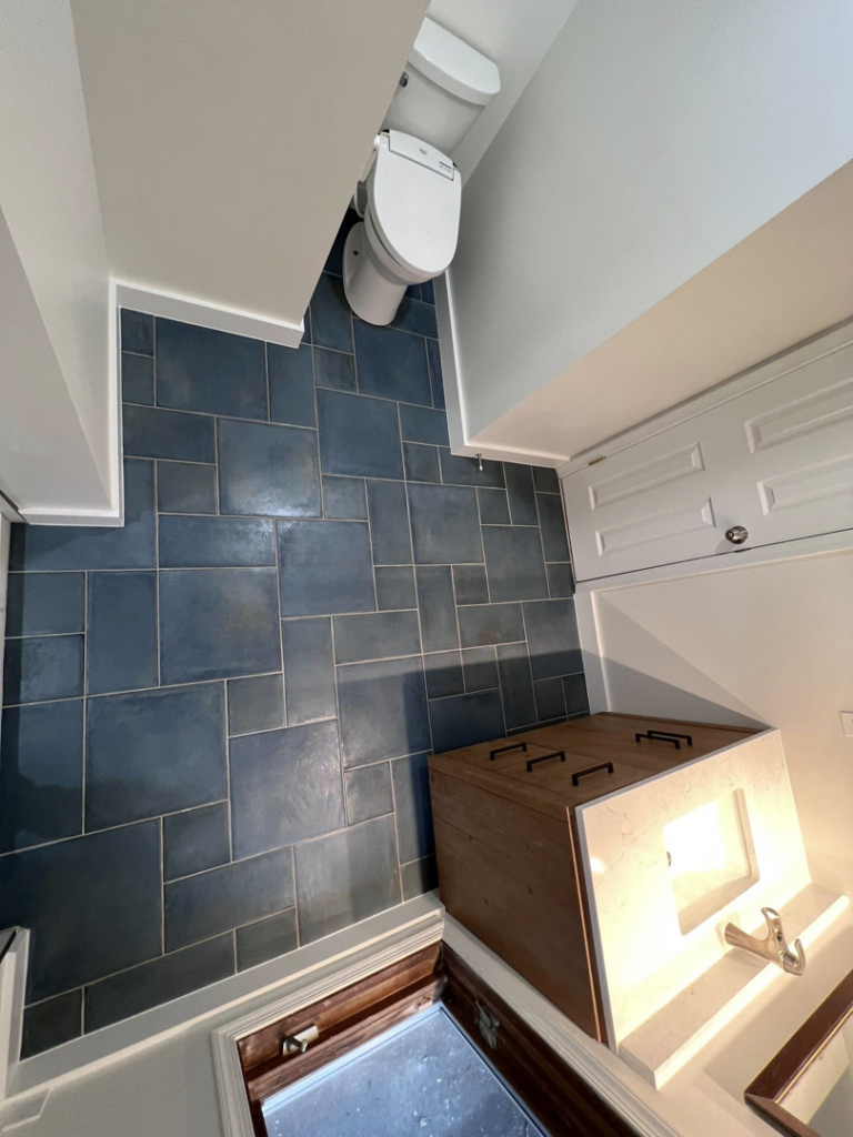 An overhead view of a newly tiled bathroom floor with dark blue tiles, a toilet, and part of a vanity, completed by Great Home Construction LLC in Annapolis, MD.