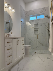 A newly remodeled modern bathroom with white vanity and marble-look tiles by Rochester Contracting in Holly Springs, NC.