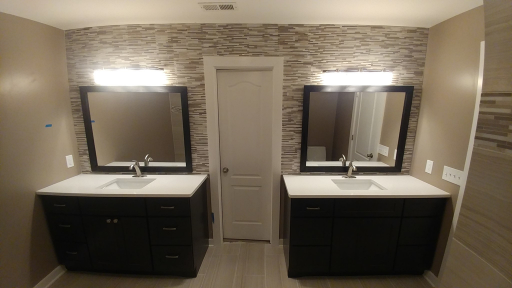 A newly renovated bathroom featuring dual vanities, mirrors, and a stylish tiled accent wall by J & J Home Improvements, LLC in Franklin, TN.