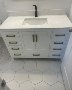 A newly installed white bathroom vanity with a sink, black faucet, and hexagon floor tiles by KACE Construction in Nashville, TN.