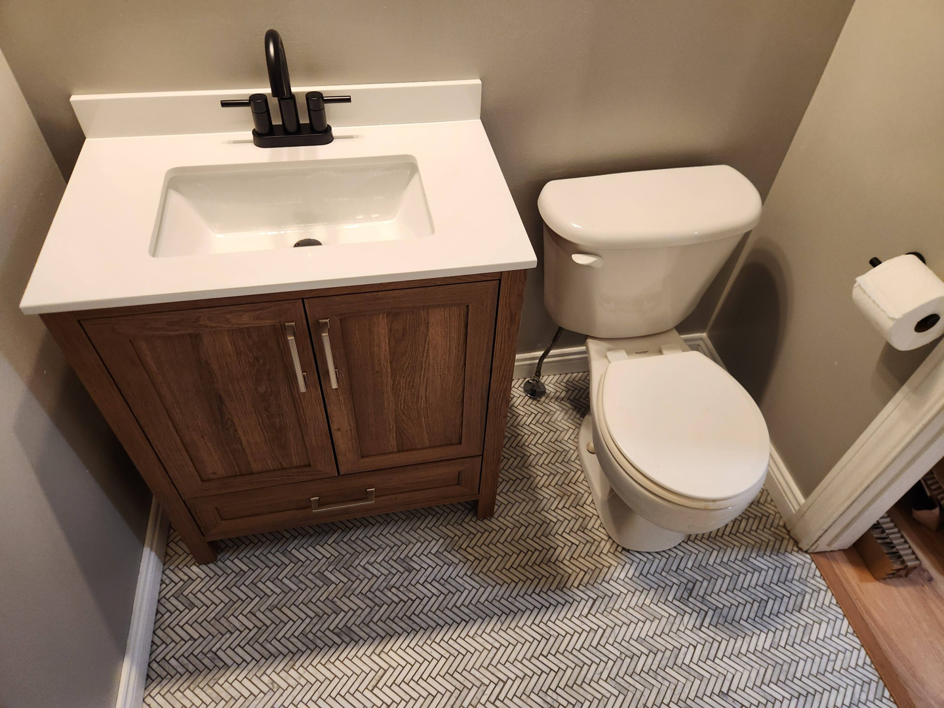 A newly installed bathroom vanity, sink, and toilet with herringbone tile flooring by SG Service, LLC in Lincoln, NE