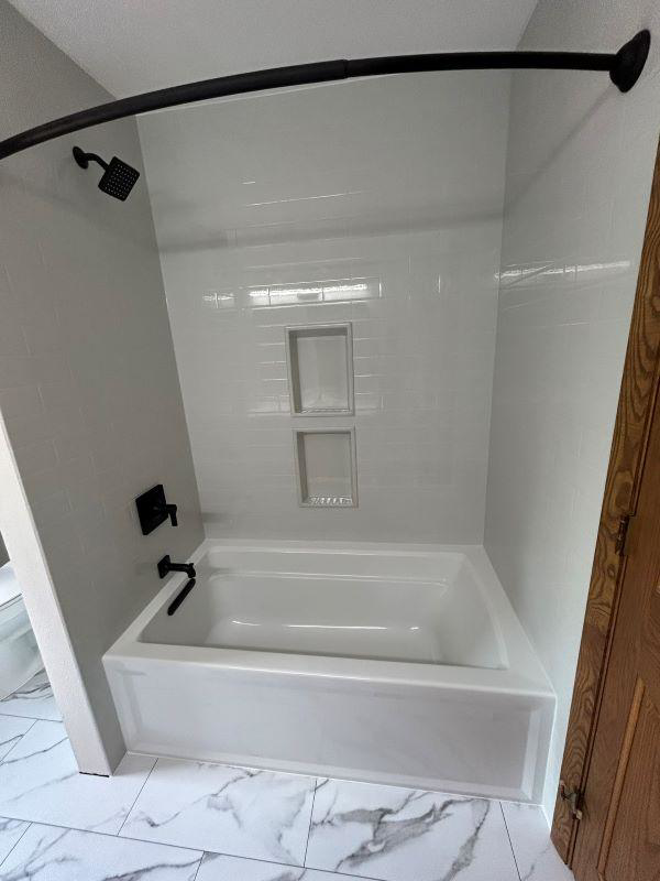 A newly installed bathtub with white tiled walls and black fixtures by VanVleet Construction in Brooklyn Park, MN.