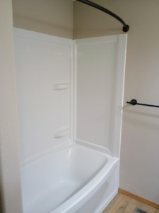 A newly installed white bathtub and shower surround with a curved rod by The Cowboy Carpenter Handyman Service LLC in Bismarck, ND.