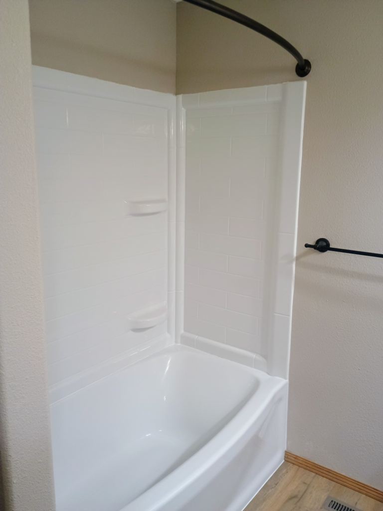 A newly installed white bathtub and shower surround with a curved rod by The Cowboy Carpenter Handyman Service LLC in Bismarck, ND.
