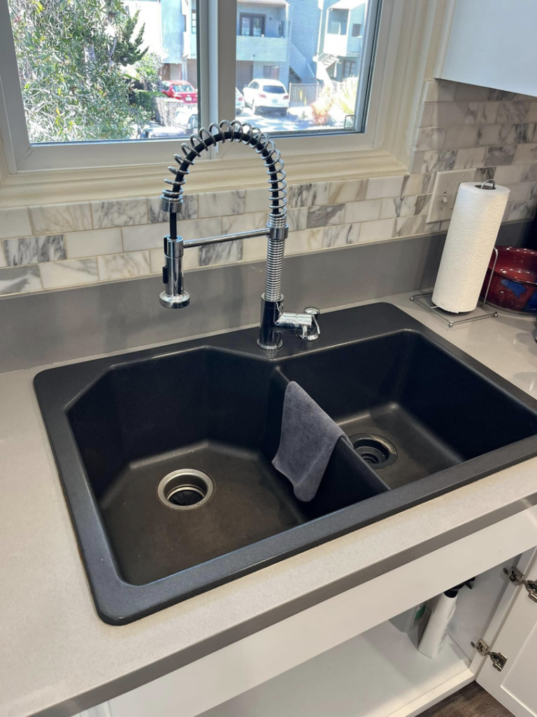 A newly installed black double kitchen sink with a pull-down faucet and marble backsplash by Pauda Handyman in San Diego, CA.