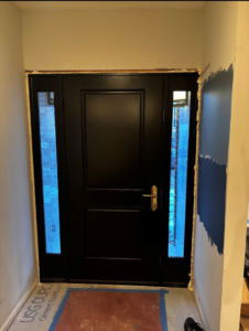 A newly installed black front door with side lights, showing ongoing renovation work by All In Service Group, LLC in Chicago, IL.