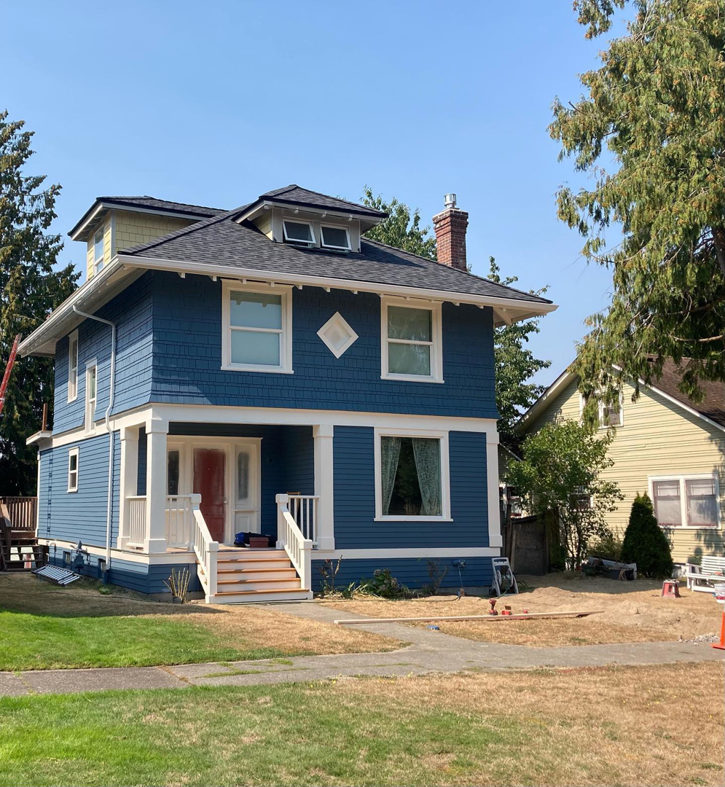 A newly renovated blue house with new siding, roof, and front steps by Nation / Phillips Construction in Tacoma, WA.