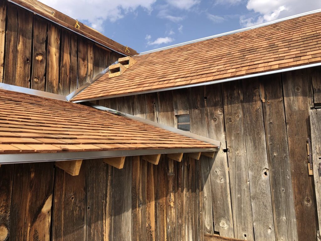Installation of new cedar shake roofing and gutters on a rustic wooden building by Deep Roots Craftsmen in Fort Collins, CO.