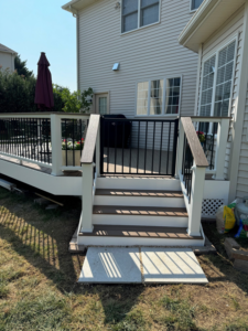 A newly constructed composite deck with stairs and a gate leading to a concrete pad by Sundecks, Inc. in Manassas, VA.