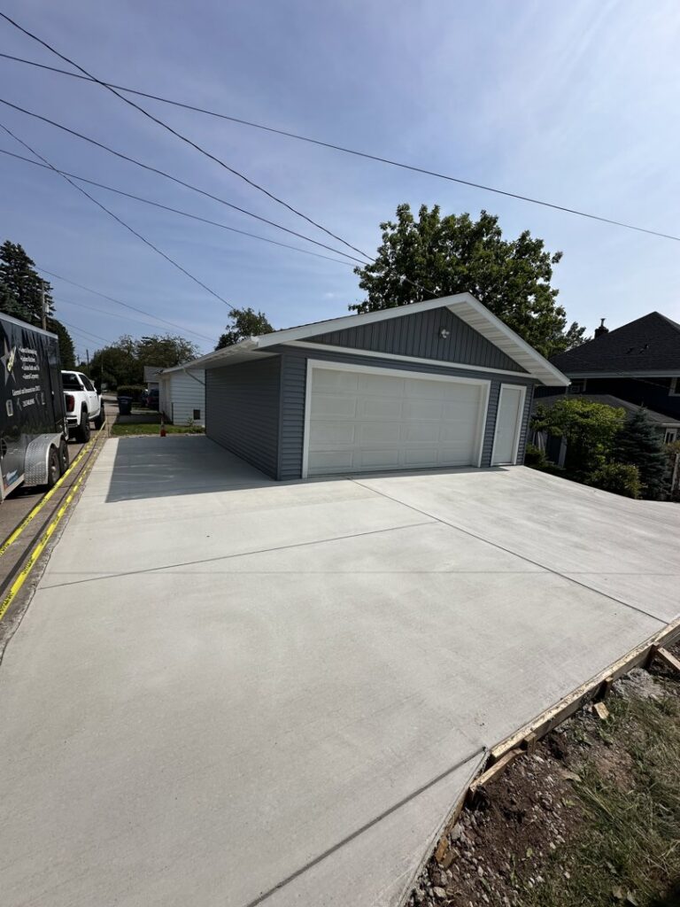 A newly poured concrete driveway leading to a garage with fresh siding, completed by Orion Construction Services in Duluth, MN.