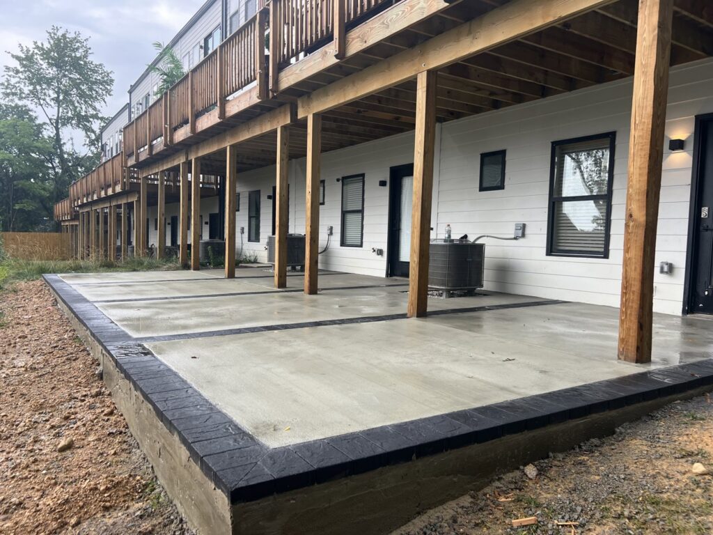 A newly poured concrete patio with decorative black borders installed under a deck by Landscape By Today in Bowie, MD.