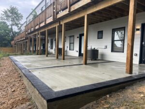A newly poured concrete patio with decorative black borders installed under a deck by Landscape By Today in Bowie, MD.
