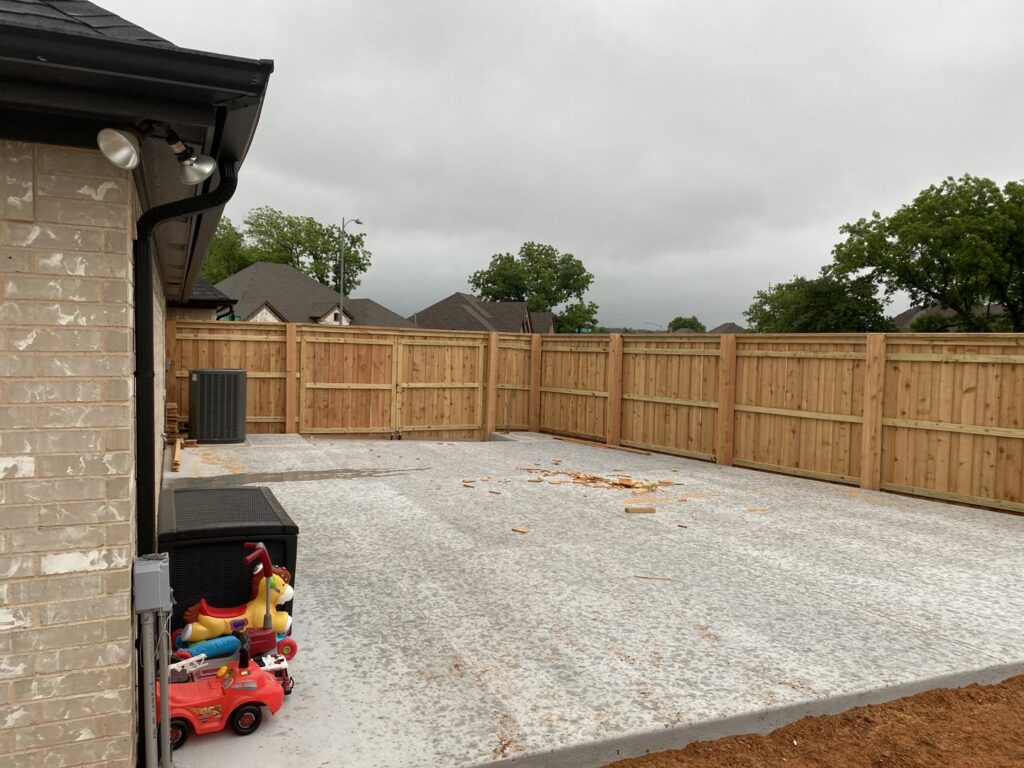 A newly installed concrete patio and wooden privacy fence in a backyard, completed by Falls Contracting, LLC in Raleigh, NC.