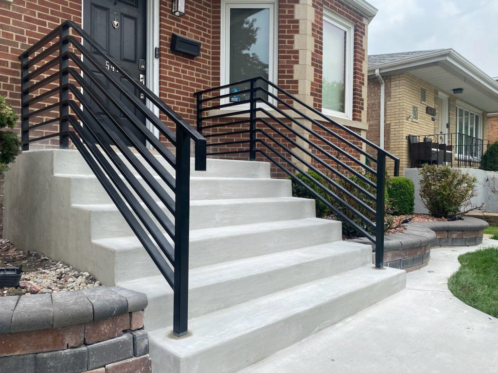 Newly installed concrete steps with modern black metal railings leading to a brick house, a project by Keeler Construction Group Inc. in Blue Island, IL.
