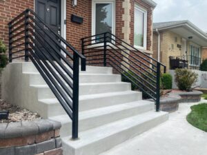 Newly installed concrete steps with modern black metal railings leading to a brick house, a project by Keeler Construction Group Inc. in Blue Island, IL.