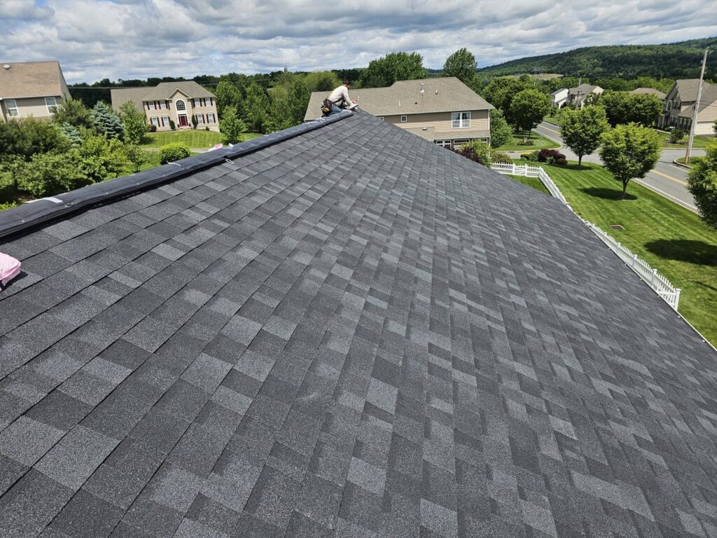 Close-up view of a newly installed dark gray shingle roof with a worker, completed by Moonshot Roofing in Columbia, PA.