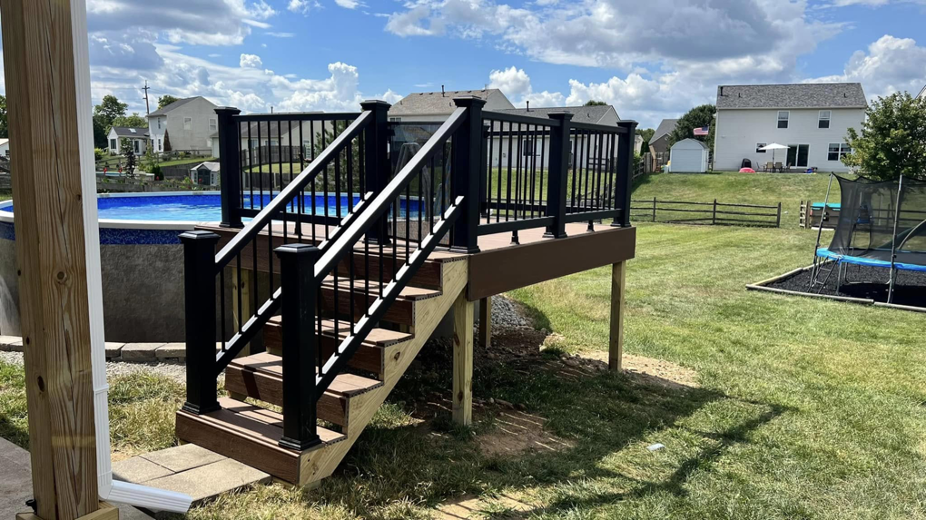 A newly installed wooden deck with black railings next to an above-ground pool by Armbruster General Contracting in Cincinnati, OH.