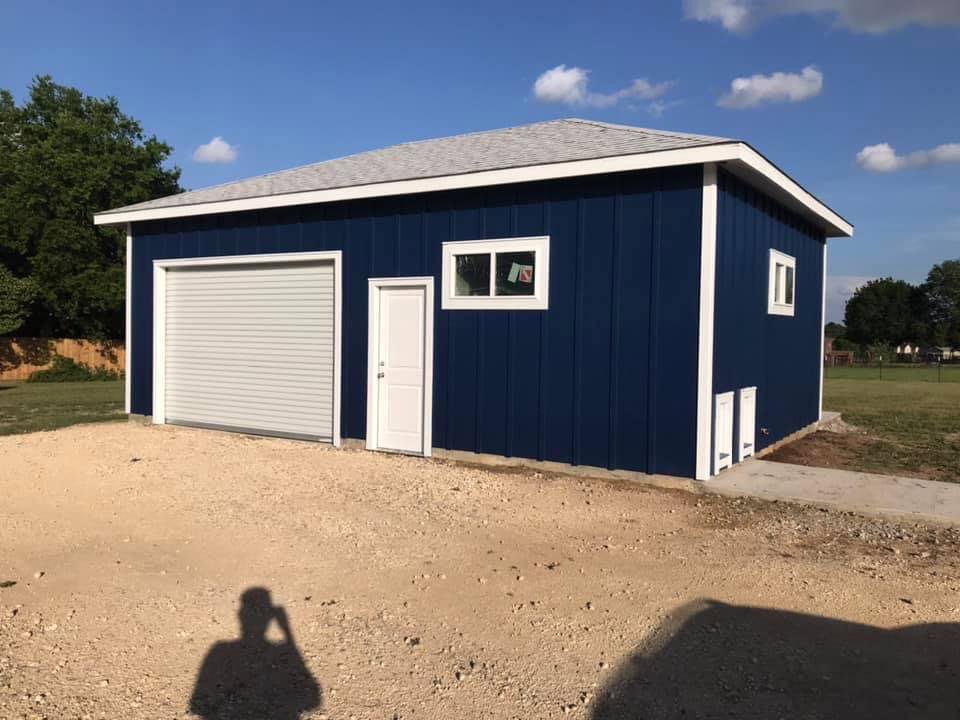 A newly constructed detached garage with blue siding and a roll-up door by Finesse Painting and Remodeling in Fort Worth, TX.