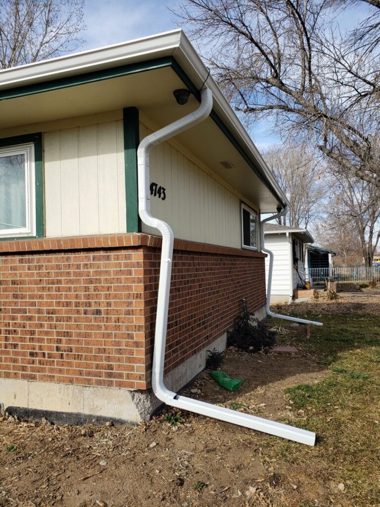 A newly installed white downspout on the side of a house, part of gutter services by Jesse Roofs Co. in Denver, CO