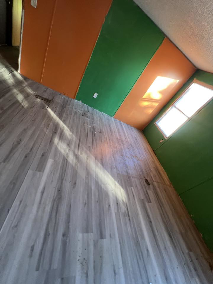 A room with newly installed laminate flooring and green and orange walls, a handyman service by Cosa Cleanouts & Junk Removal in Topeka, KS.
