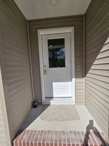 A newly installed white front door with a window and light-colored siding by Shore Home Construction Roofing in Salisbury, MD.
